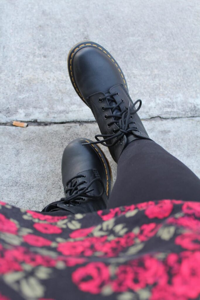 Bottes noires, leggings, jupe fleurie sur trottoir gris.