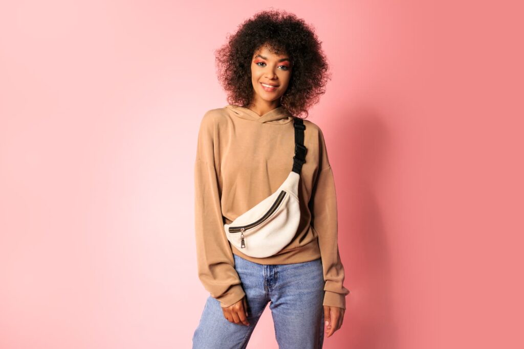 Femme portant sweat beige et sac banane blanc.