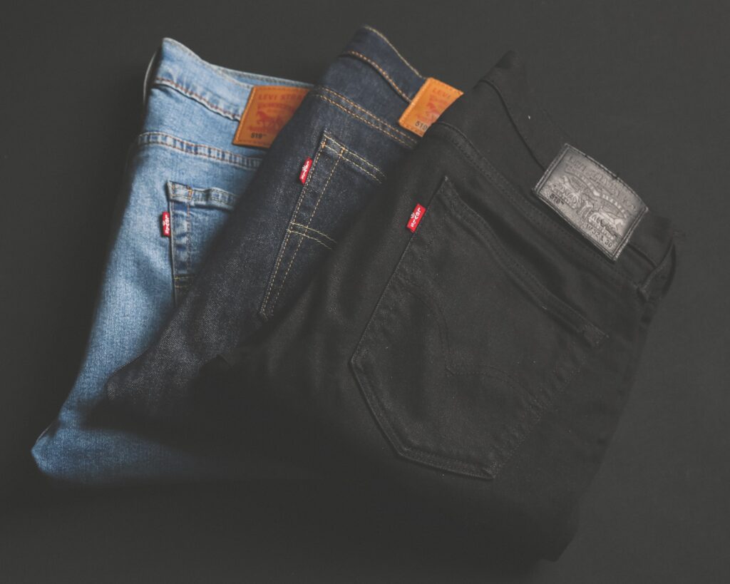 Trois paires de jeans de marque, l'une en denim bleu clair, la seconde en bleu indigo et la troisième en noir, empilées sur un fond sombre.