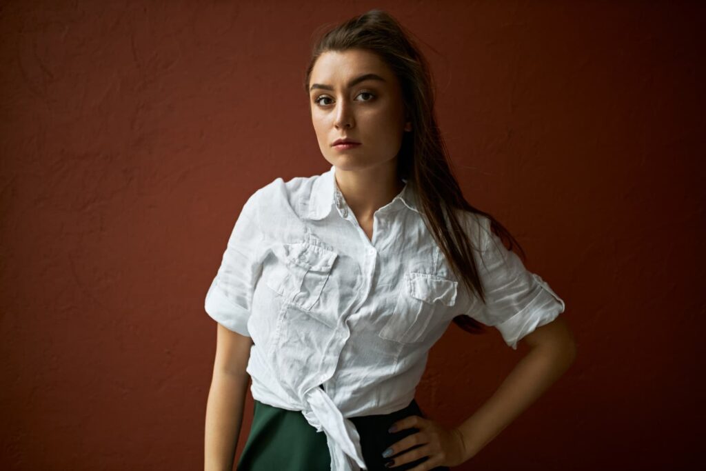 Femme en chemise blanche devant mur brun.