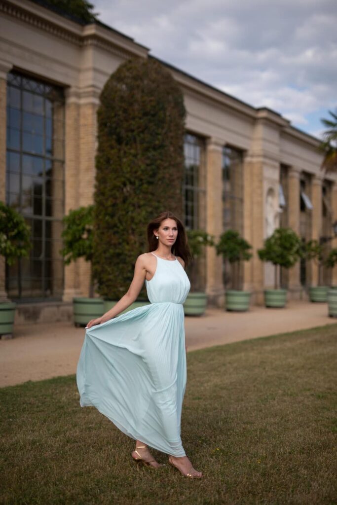 Femme en robe turquoise devant un bâtiment historique.