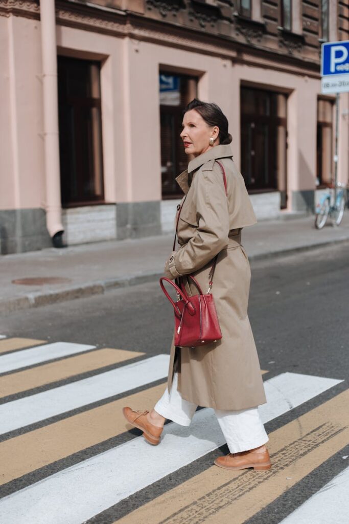 Stylish senior woman in a trench coat crossing a city street on a zebra crossing.